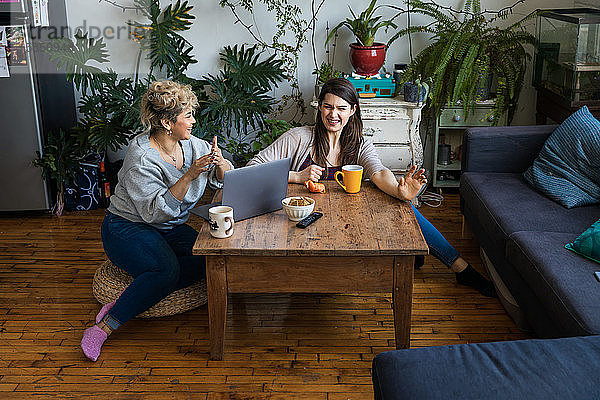 Glückliche Freunde unterhalten sich bei Tisch mit Kaffeetassen und Laptop