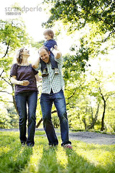 Vater hält Sohn im Park auf den Schultern  während Mutter aufschaut