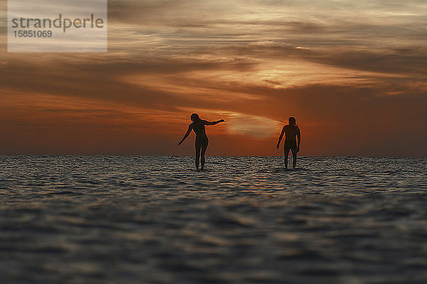 Zwei Surfer im Ozean bei Sonnenuntergang