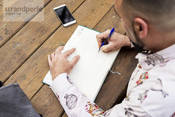 Junger bärtiger Geschäftsmann sitzt am Tisch und macht Notizen in einem Notizbuch