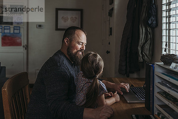 Vater mit junger Tochter im Vorschulalter sitzt  während er arbeitet