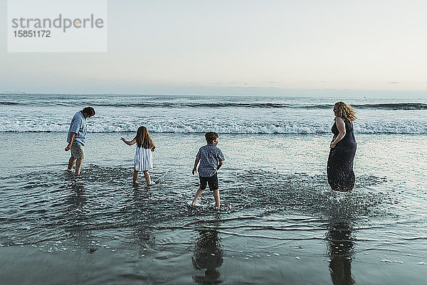 Vierköpfige Familie  die in der Abenddämmerung im Meer spielen und sich gegenseitig bespritzen