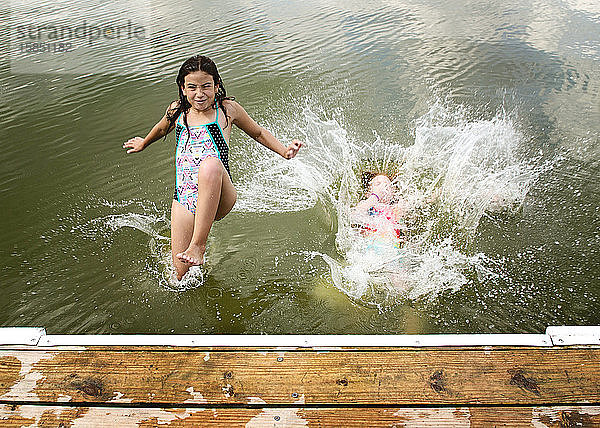 Zwei junge Mädchen in Badeanzügen springen von einem Dock in einen See