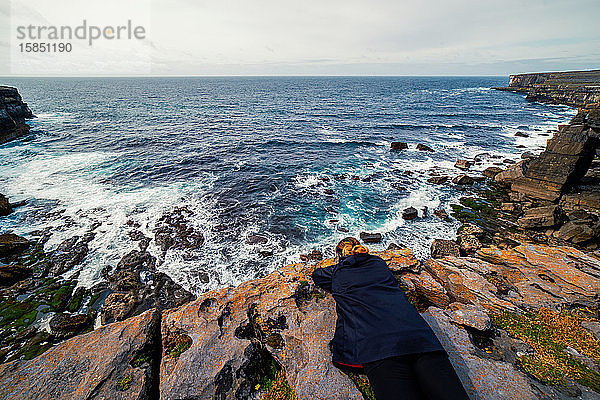 Hochwinkelaufnahme einer Frau  die auf einer Klippe mit Blick auf den Ozean liegt