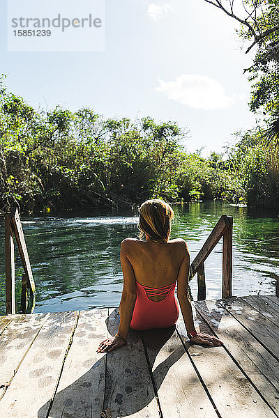 Rückenansicht einer attraktiven Frau  die in Cenote auf einem Holzpieker sitzt