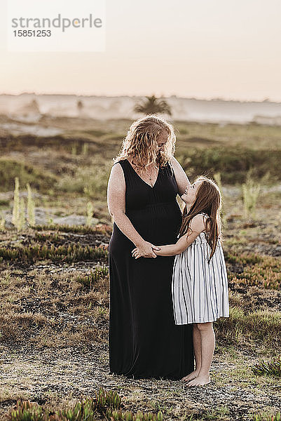 Porträt einer rothaarigen Mutter  die ihre kleine Tochter bei Sonnenuntergang am Strand umarmt