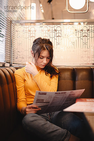 Teenagerin betrachtet Speisekarte  während sie im Restaurant sitzt