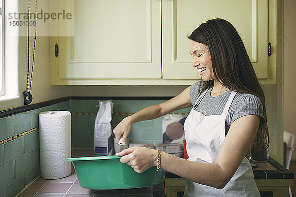 Lächelnde Frau  die in der Küche Essen in einem Behälter verquirlt