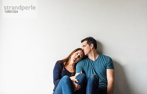 Ausgeschnittenes Bild eines liebenden Paares  das zusammen an einer weißen Wand sitzt.