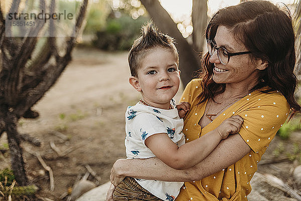 Mutter hält jungen Sohn und lächelt in hinterleuchtetem Kaktusgarten