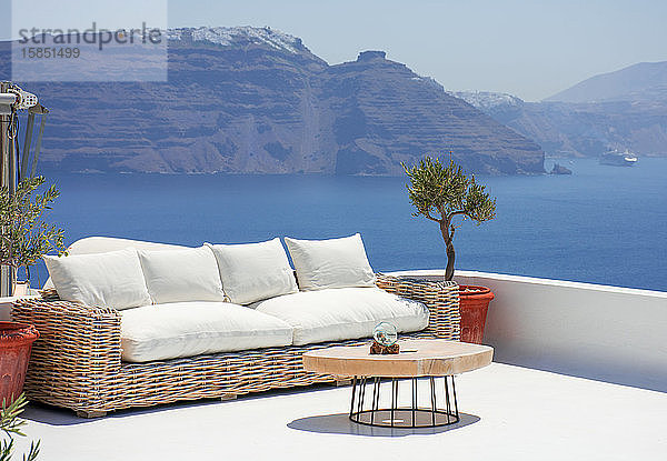 schöne Terrasse mit Couch und einem kleinen Tisch im Dorf Oia auf der griechischen Insel Santorin. Niemand genießt jetzt den spektakulären Panoramablick auf die Klippen mit der Fira an der Spitze. Hori