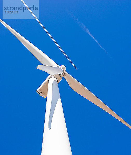 Windturbine vor blauem Himmel mit einem über uns vorbeifliegenden Düsenflugzeug