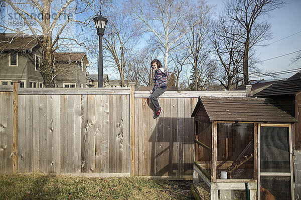 Ein lächelndes glückliches Kind sitzt an einem kühlen Frühlingstag auf einem Zaun