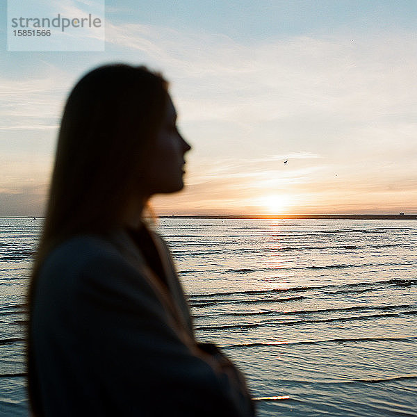 Schöne Frau steht am Meer und genießt den Sonnenuntergang