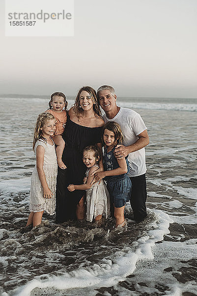 Porträt einer jungen Familie mit nassem Haar  die bei Sonnenuntergang im Meer steht