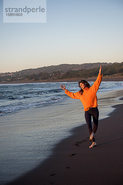 Eine Frau tanzt bei Sonnenuntergang entlang der Küste