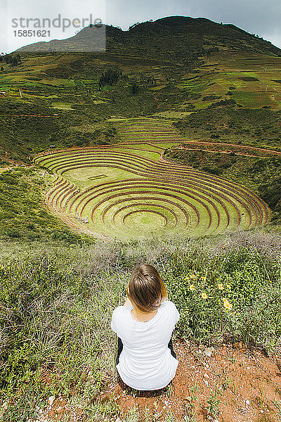 Eine junge Frau sitzt in der Nähe des berühmten peruanischen Fleckens Moray in Peru