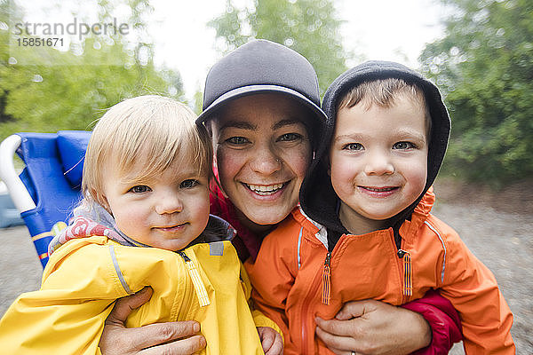 Porträt einer Mutter mit ihren beiden Kindern mit Regenjacken.