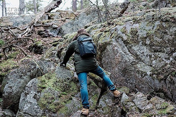Mann klettert im Winter auf einen Felsen  während er in einem Wald wandert