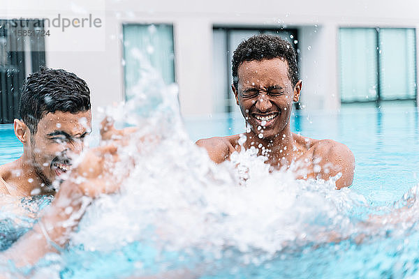 Mann lächelt mit geschlossenem Mund  während er mit seinen Freunden im Wasser eines Schwimmbeckens spielt