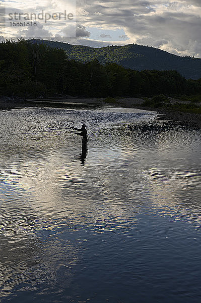 Ein Fliegenfischer  der abends auf einen Fluss wirft.