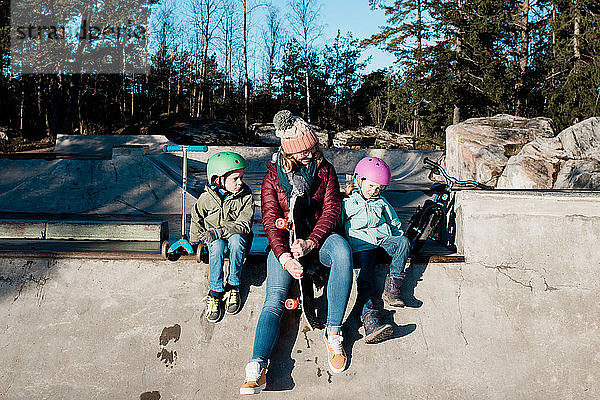 Mama und ihre Kinder spielen in einem Skatepark draußen in der Sonne