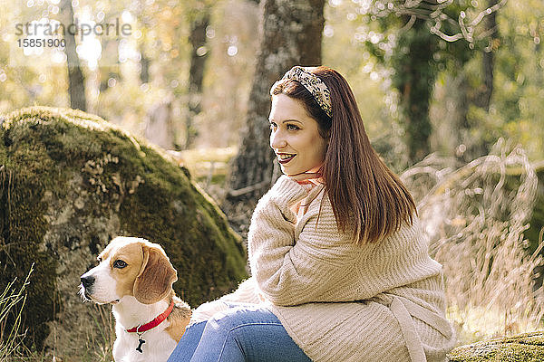 Lächelnde junge Frau  die während eines Spaziergangs neben ihrem Hund sitzt