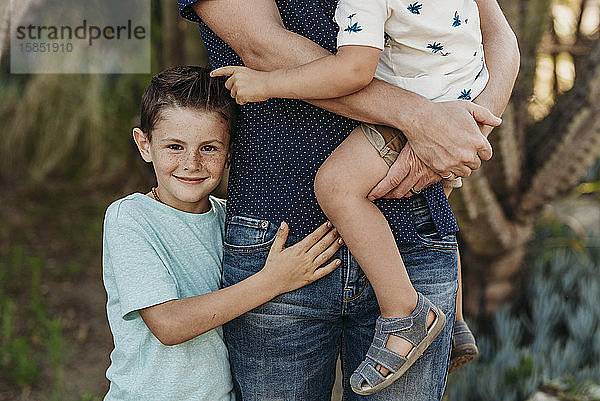 Halbansicht eines Jungen im Grundschulalter  der Vater und Bruder umarmt und lächelt