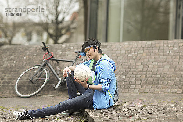 junger Mann mit Ball im Freien sitzend