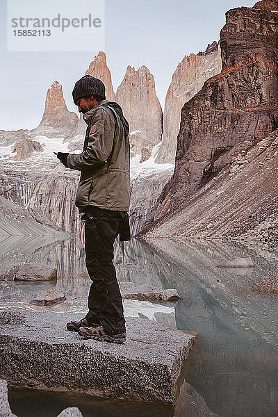 Wanderer in den Bergen überprüft sein Telefon in der Nähe eines ruhigen Sees