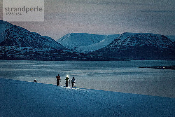 Eine Gruppe von 3 Personen fährt bei Sonnenaufgang Ski  dahinter Meer und Berge