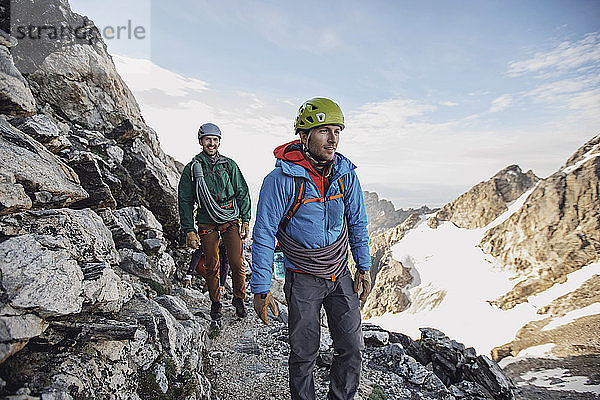 Zwei Felskletterer mit Helm und Seilen gehen an einer Klippe in Tetons entlang