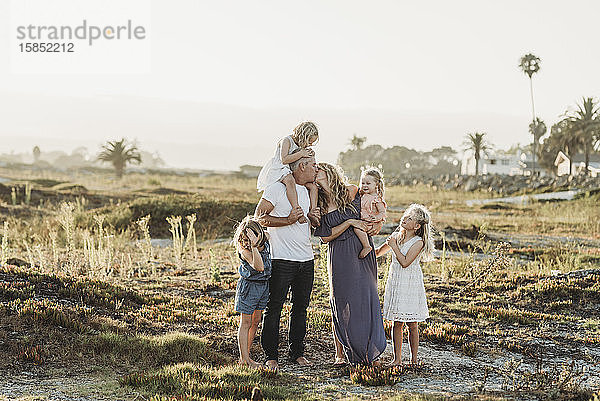 Lifestyle-Porträt einer Familie mit jungen Mädchen  die sich bei Sonnenuntergang am Strand küssen