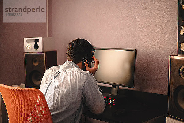 Konzentrierter Mann hört Musik über Kopfhörer am Computer sitzend