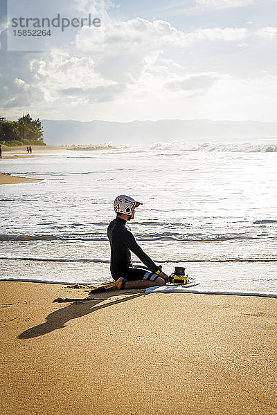 Ein Surffotograf sitzt auf dem Sand und schaut auf das Meer