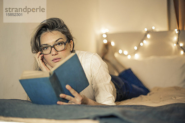 junge Frau liest ein Buch auf einem Bett