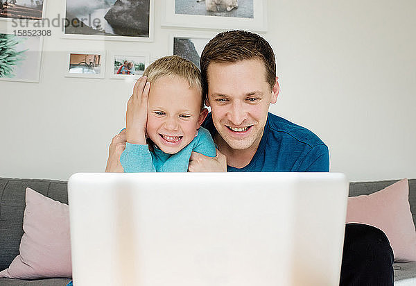 Vater und Sohn lachen zu Hause  während sie zu Hause auf einen Laptop schauen