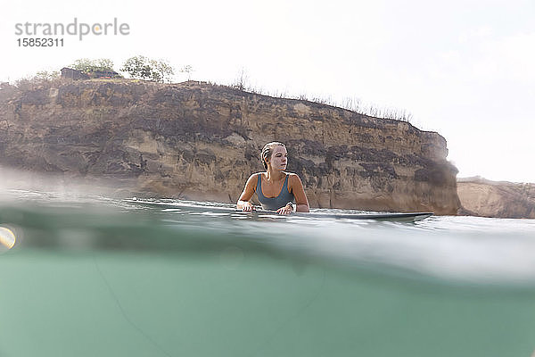 Glückliche Frau sitzt auf einem Surfbrett im Meer