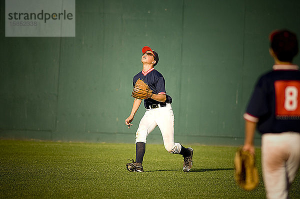 junger Baseballspieler mit Sonnenbrille  der zu einem Flugball aufschaut