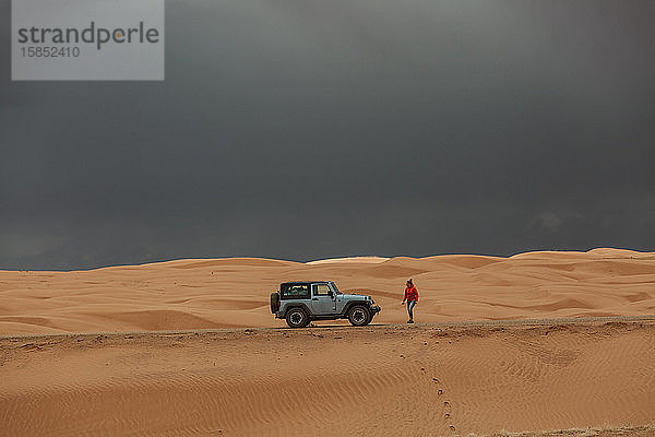 Frau geht unter stürmischem Himmel in den Sanddünen von Utah zurück zum Jeep