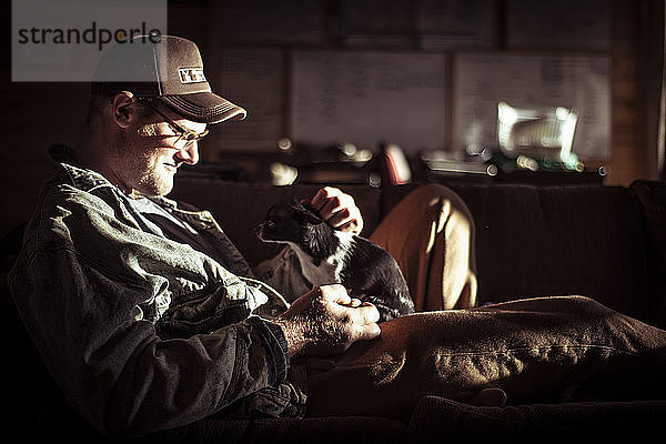 großer Bauernmann sitzt in der Morgensonne mit winzigem Chihuahua-Hund