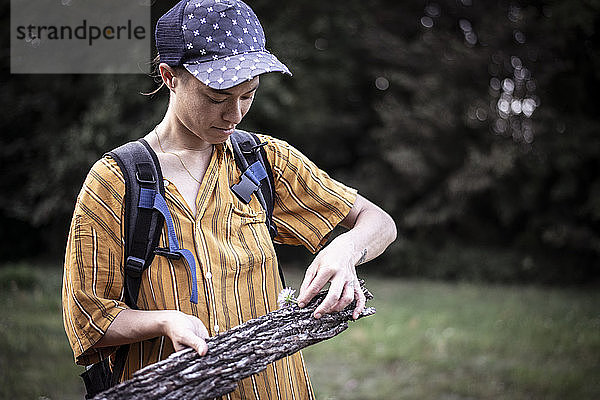 androgynes Mädchen mit Mütze spielt mit Blumen und Baumrinde im grünen Park