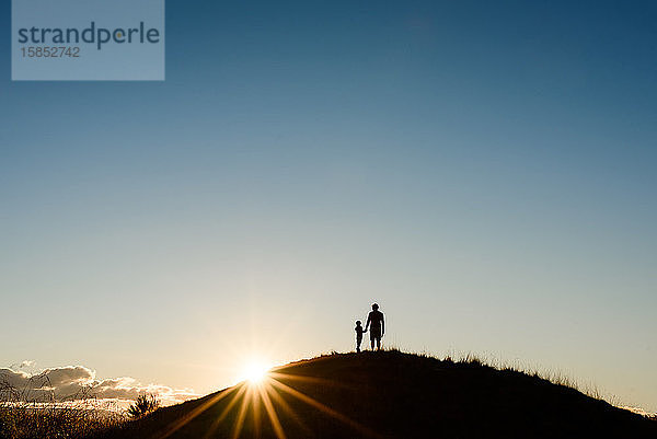 Silhouette von Vater und Sohn auf der Spitze eines Hügels bei Sonnenuntergang