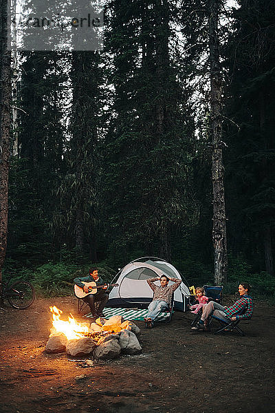 Eine Gruppe von Freunden sitzt beim Zelten in Oregon um ein Lagerfeuer herum.
