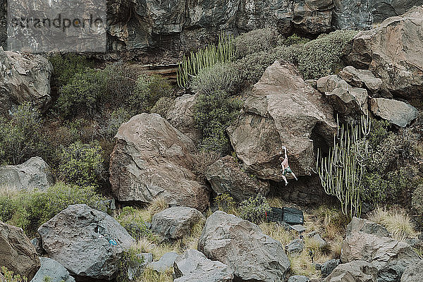 Mann klettert auf einen Felsbrocken inmitten einer Vulkanlandschaft