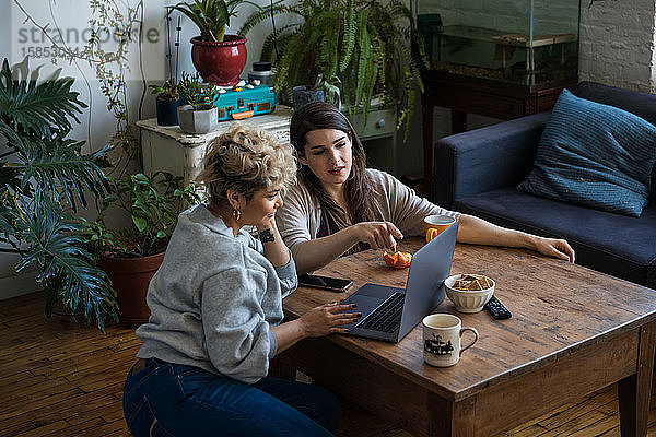 Hochwinkelansicht einer Frau  die auf einen Freund zeigt  während dieser einen Laptop am Tisch im Wohnzimmer benutzt