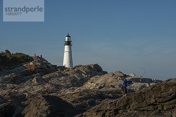 Eine Frau beim Fliegenfischen in der Nähe eines Leuchtturms an der Küste von Maine