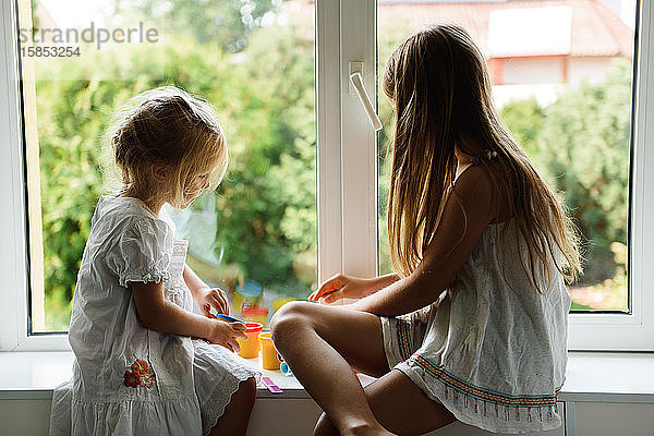 Zwei Schwestern spielen Knetmasse am Fenster