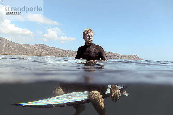 Porträt eines glücklichen Mannes  der auf einem Surfbrett im Meer posiert