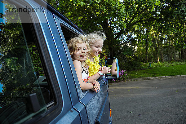 zwei junge Mädchen  die lächeln und sich aus dem Autofenster lehnen